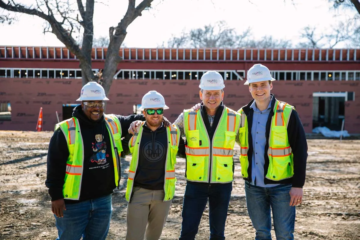 4 guys in hardhats and reflective vests in front of job site