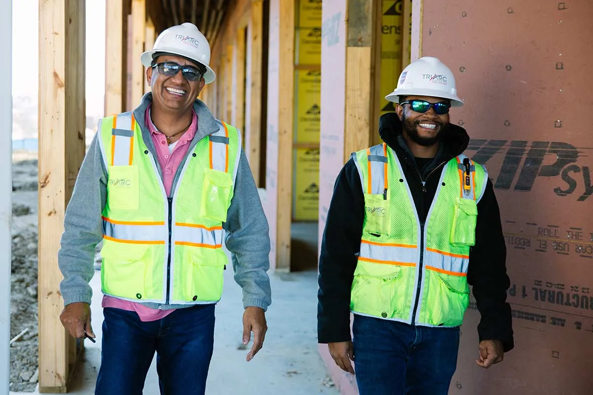 2 guys in hardhats and reflective vest standing in job site.